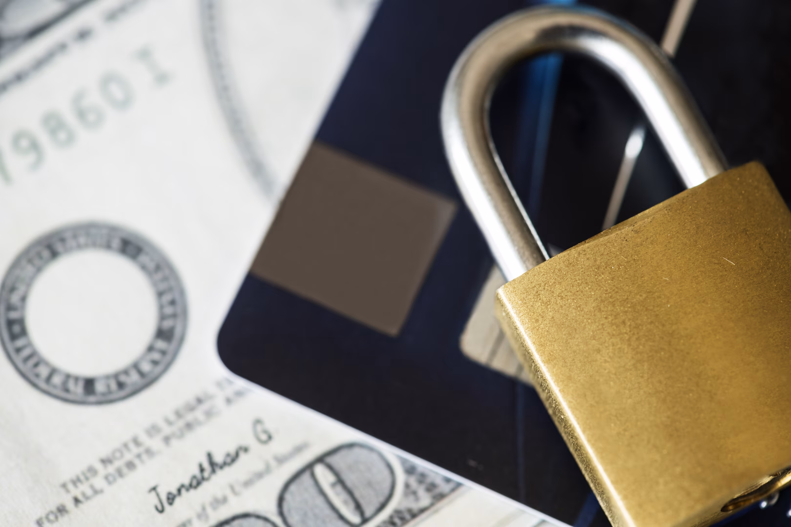 A lock sitting on top of a credit card and a 100 dollar bill.